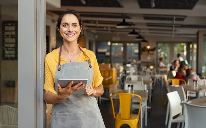 A restaurant owner standing in the doorway of her venue holding a tablet